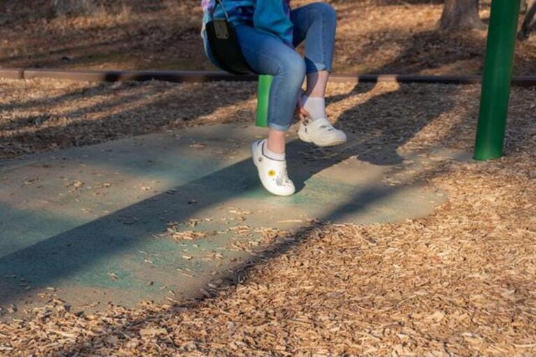 A girl adjusting removing her sling back shoes before swinging on a playground in Newport News Park.