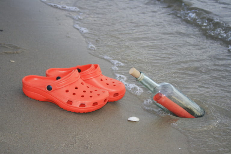 pair of red crocs and red letter as message in a bottle at a sandy beach