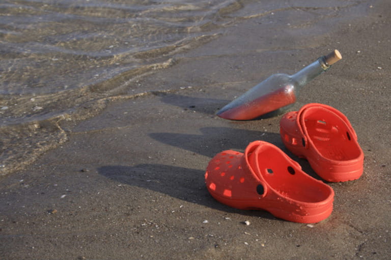 pair of red crocs and red letter as message in a bottle at a sandy beach