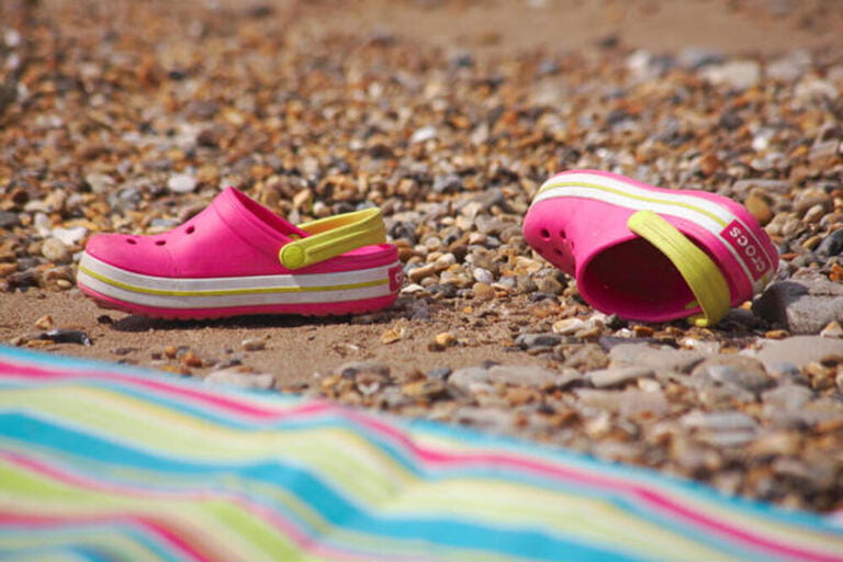pink crocs discarded on beach next to stripey beach towel