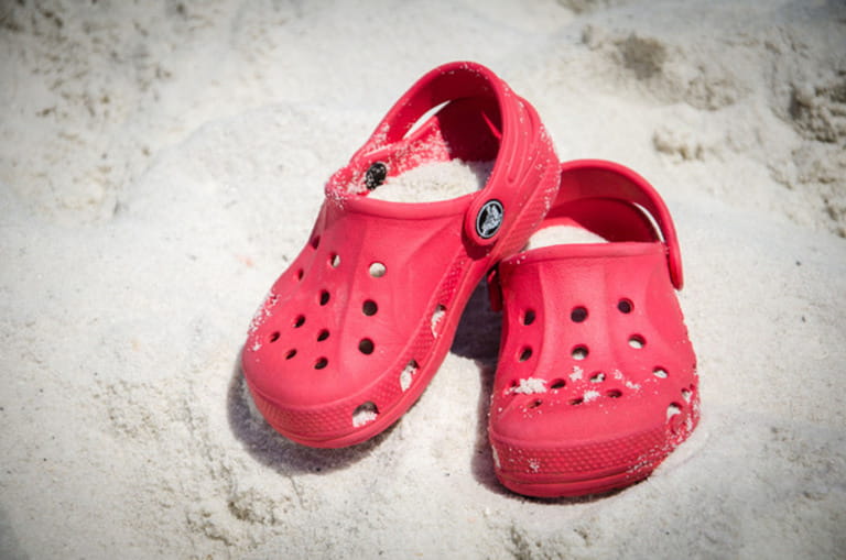 Pair of Crocs shoes covered in sand on the beach