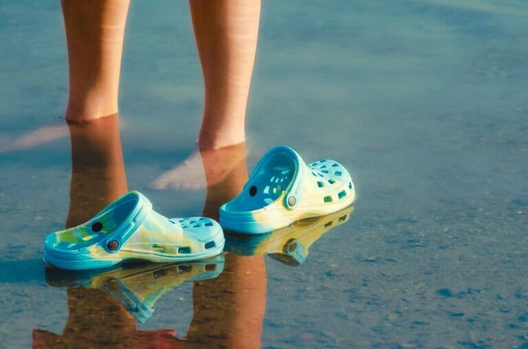 crocs sandals floating in clear water next to female feet close up