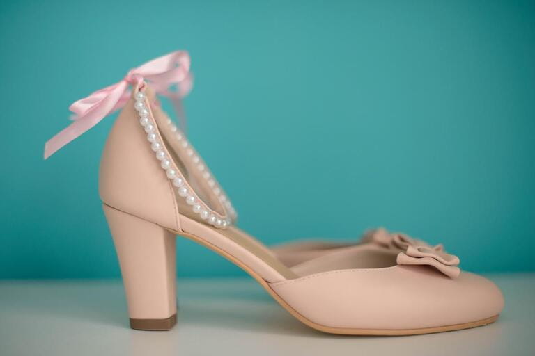 Side view of a beige leather chunky mid heel women shoes with delicate bow an pearls strap against a teal background. Elegant women footwear for formal occasion or day-to-day wear. Side view of a beige leather chunky mid heel women shoes with delicate bow an pearls strap against a teal background. Elegant women footwear for formal occasion or day-to-day wear.