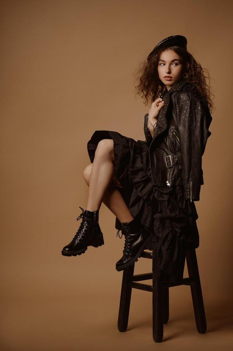Autumn fashion conception: confident curly brunette woman wearing total black outfit with beret, leather biker jacket, dress, lace up chunky sole ankle boots.