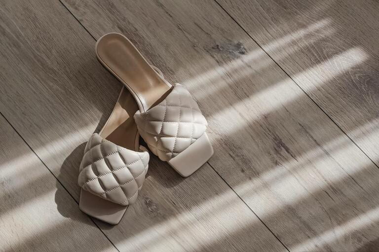 Modern feminine summer sandals, flops of beige color on the floor with natural morning sunlight Modern feminine summer sandals, flops of beige color on the floor with natural morning sunlight