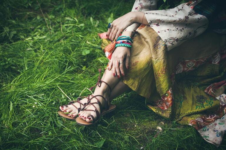 woman legs on grass in strap flat sandals and boho style silky dress with lot of bracelets on hands