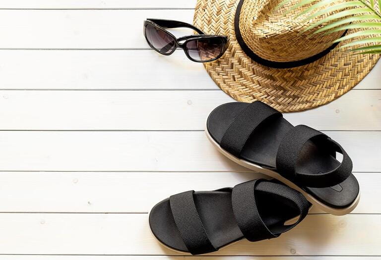 Women's open-toe black sandals from recycled plastic fibers, straw hat, sunglasses on the wooden boardwalk. Summer traveling concept. Women's open-toe black sandals from recycled plastic fibers, straw hat, sunglasses on the wooden boardwalk. Summer traveling concept.