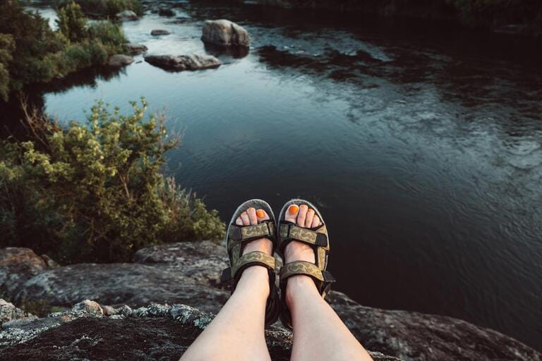 Traveler woman hiking sandals on mountain near river on nature background. Trekking female shoes. Travel healthy active lifestyle. 