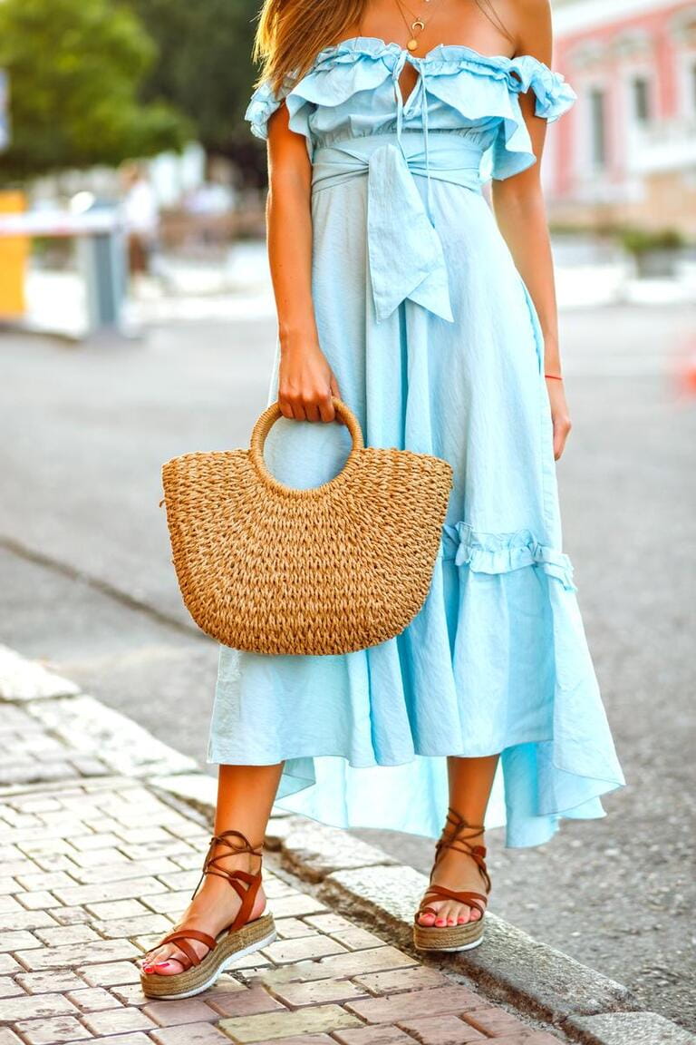Street fashion details of stylish elegant woman wearing trendy blue vintage ruffle dress, gladiator sandals and straw bag, summer vacation relaxing style.