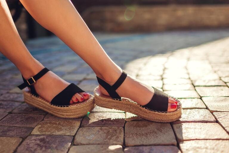 Stylish woman wearing black summer shoes with straw sole outdoors. Comfortable slippers. Fashion beauty.