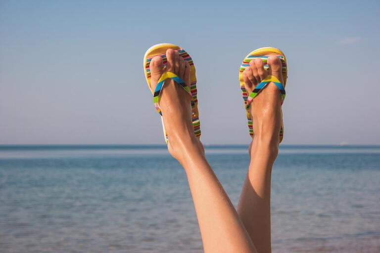 Female legs and sea. Feet in colorful flip flops. Away from bustle and noise. Get a tan.