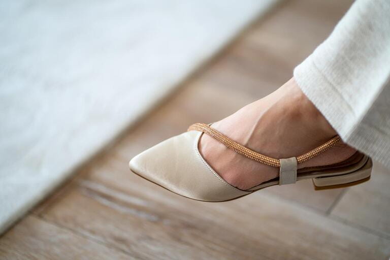 Close-up of left foot of young woman wearing pointed and yellow detailed ballet flats