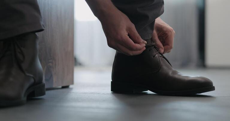 young man lace up his brown leather chukka boots indoor young man lace up his brown leather chukka boots indoor