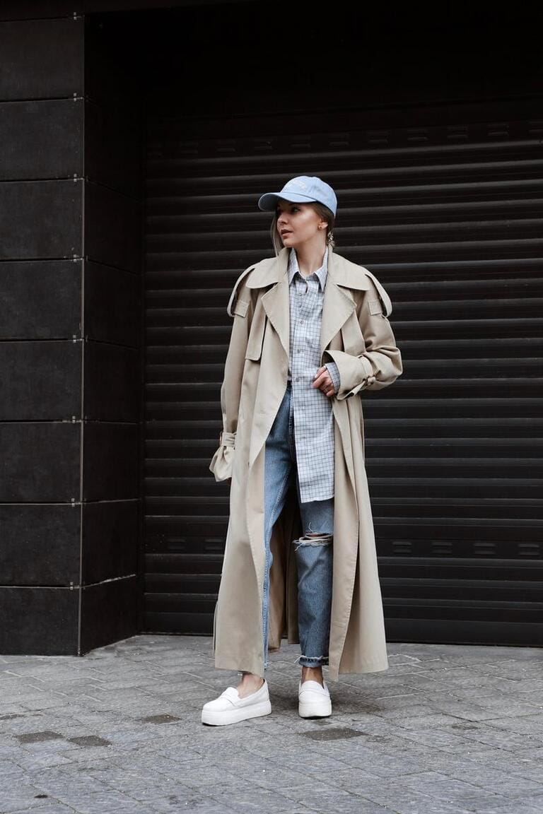beautiful blonde girl dressed in beige trench coat, blue jeans, checkered shirt and cap, white sneakers, bag in hand, accessories, stylish fashion outfit, full length lifestyle model beautiful blonde girl dressed in beige trench coat, blue jeans, checkered shirt and cap, white sneakers, bag in hand, accessories, stylish fashion outfit, full length lifestyle model