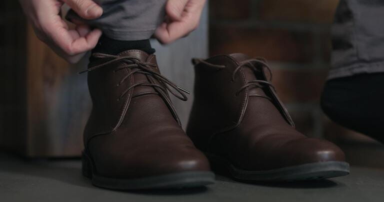 young man lace up his brown leather chukka boots indoor young man lace up his brown leather chukka boots indoor