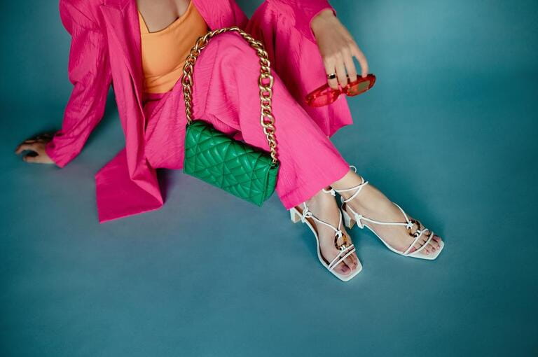 Fashion details: trendy green quilted leather bag with chunky chain, white strappy sandals, pink fuchsia color suit. Stylish woman outfit, accessories.