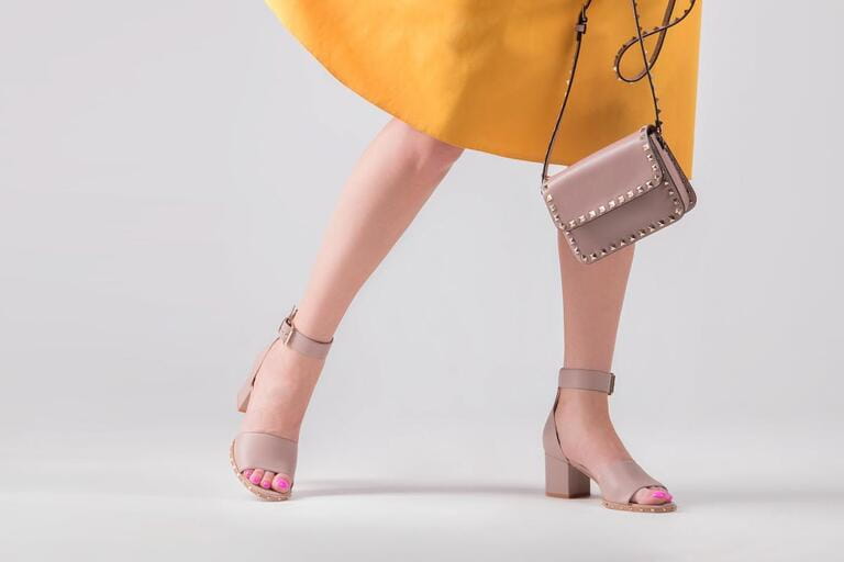 A girl wearing sandals with heels and a bag in her hand. Fashionable set of handbags and shoes.