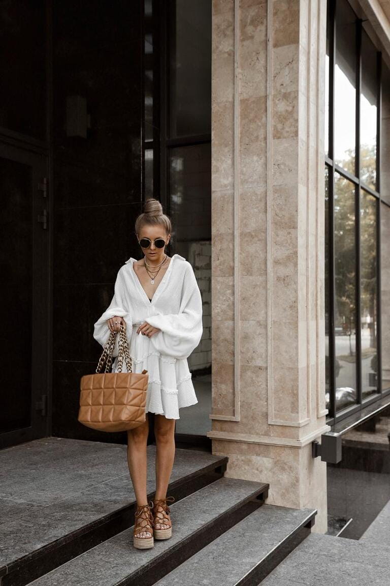 beautiful blonde girl dressed in white oversized magnificent dress, brown lace-up sandals, bag, accessories, sunglasses, bundle hairstyle, stylish summer fashion outlook, full length lifestyle model