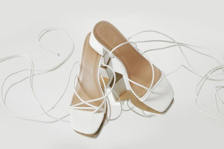 Creative studio shot of white strappy lace up block heel sandals