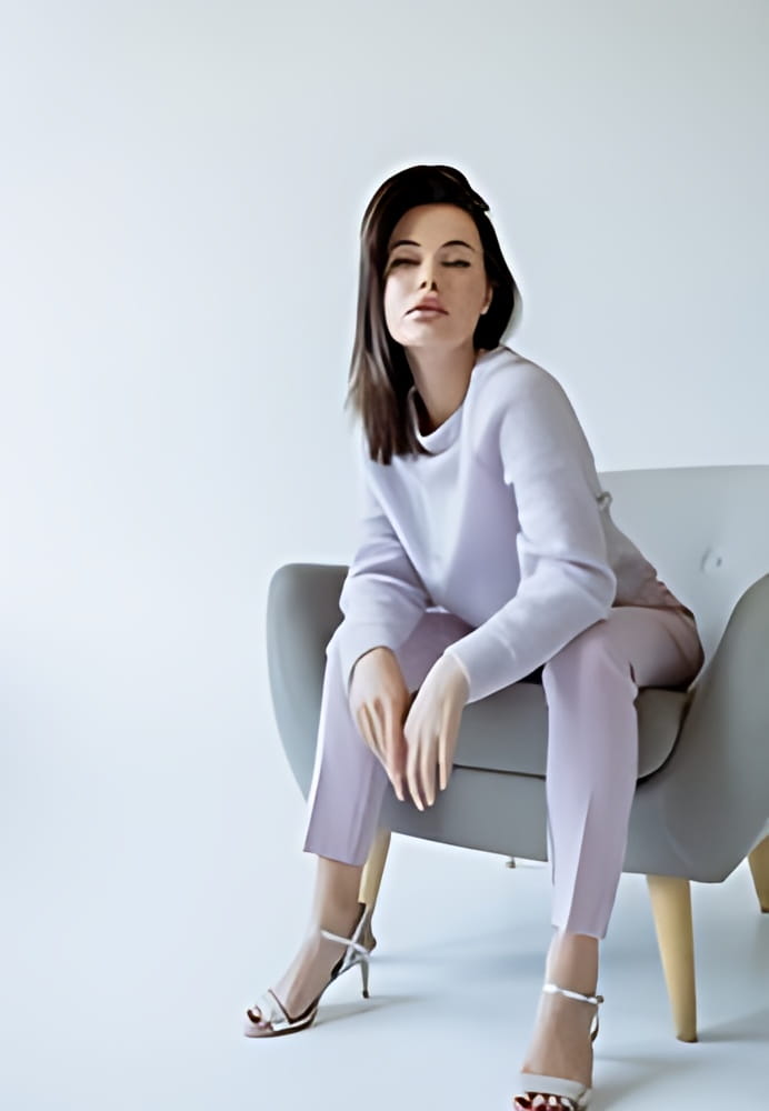 sensual brunette woman in knitted sweater and pants sitting in armchair and looking at camera on grey background sensual brunette woman in knitted sweater and pants sitting in armchair and looking at camera on grey background
